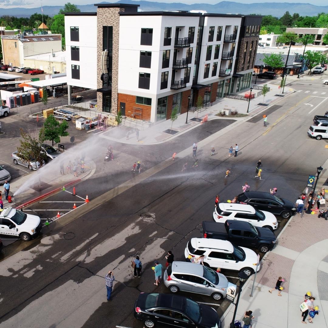 Aerial view of a fire hydrant demonstration. Water is flowing rapidly up and out of the fire hydrant and kids play in the water flow.